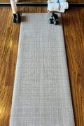 Swankymat Sloane Dust Studio Mat rolled out full-length on a wood floor with dumbbells at one end — a rollable, non-toxic high-density foam exercise mat for yoga, pilates, and HIIT in a neutral Dust crosshatch.