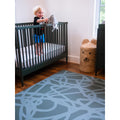 Smiling toddler in crib next to Swankymat blue abstract exercise mat and play mat in modern nursery room.